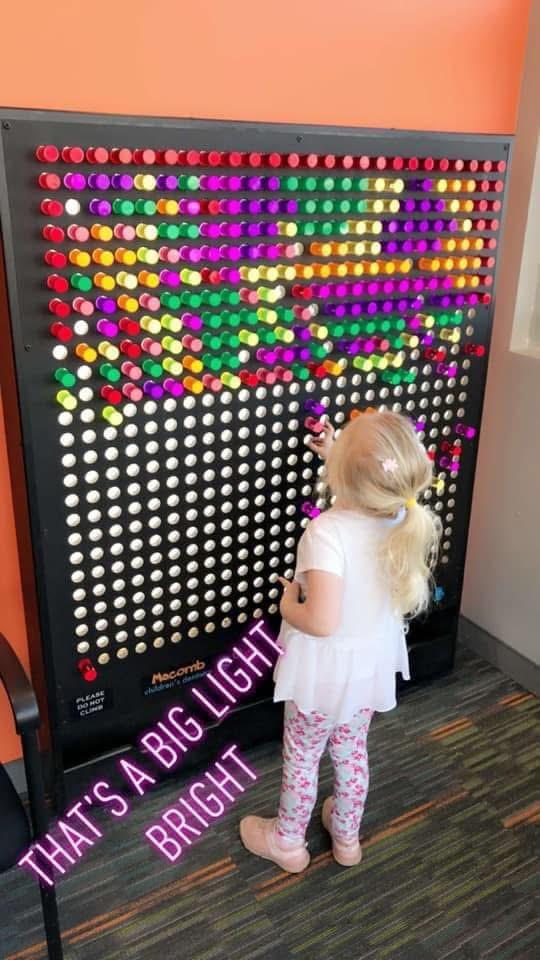 Child playing with a large wall-mounted light-up pegboard game in the office