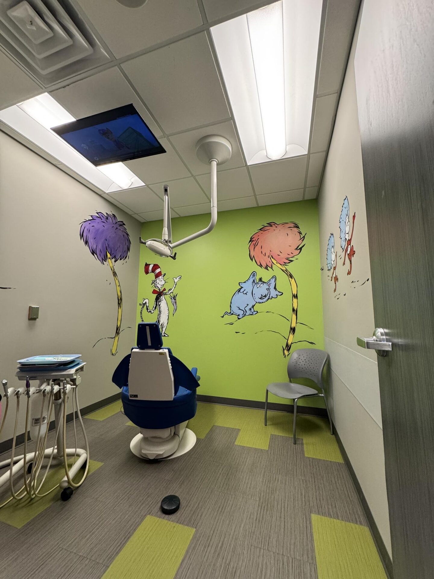 Private treatment room decorated with a Cat in the Hat and Thing 1 & Thing 2 mural, dental chair, and mounted TV